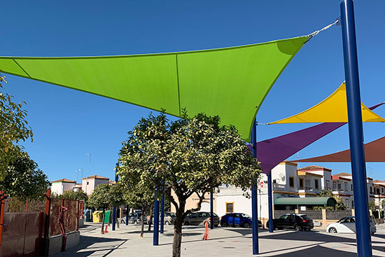 Colorful tension sail shade structure installation in a small town square.